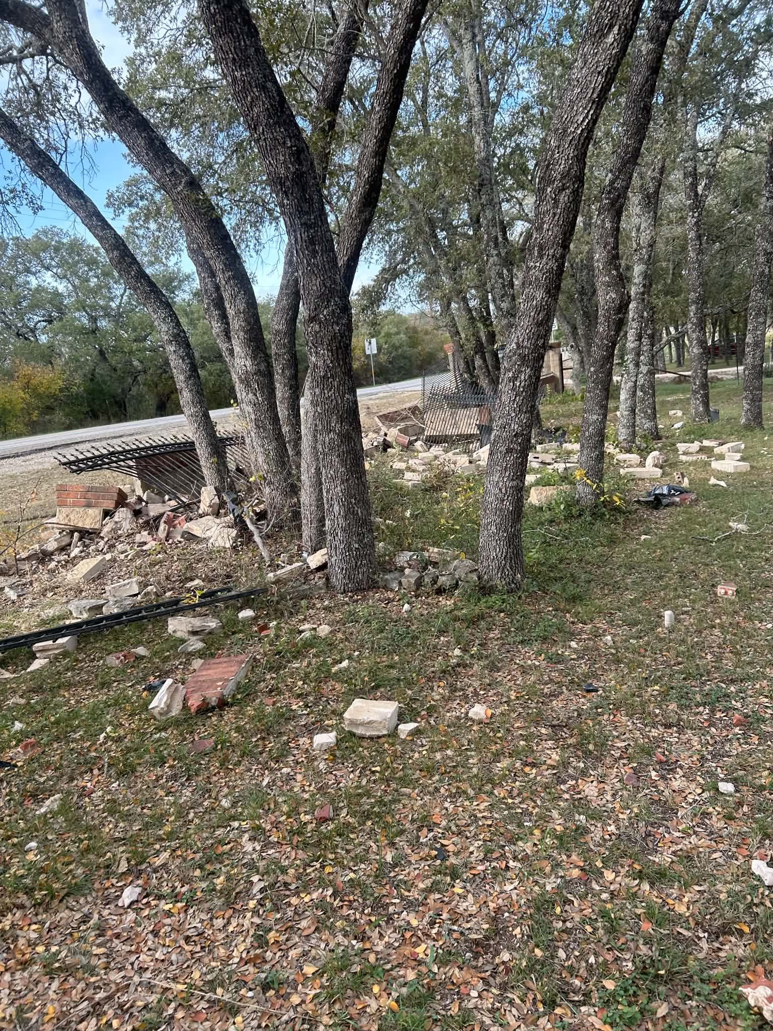 Broken stone and brick fence columns and iron fence panels scattered under oak trees