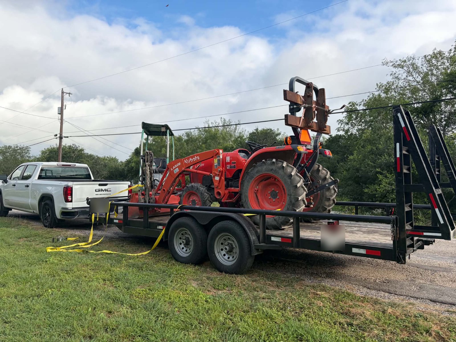 Kubota tractor strapped to an equipment trailer behind a pickup